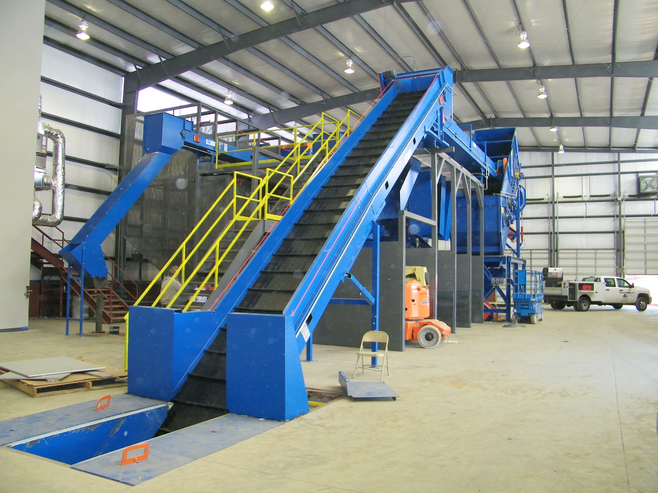 Blue Remcon sorting-line conveyors with yellow access stairs inside a recycling facility.